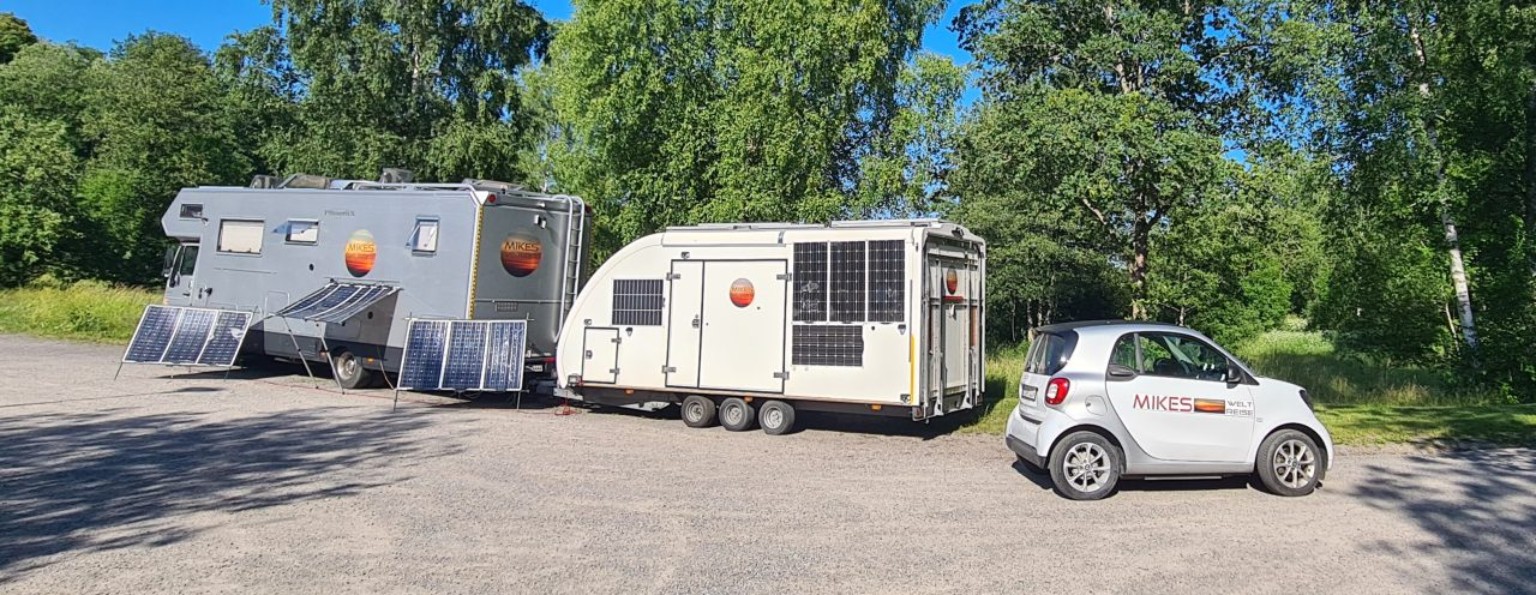 Lebensmobil mit Anhänger und Smart auf einem Stellplatz im Grünen